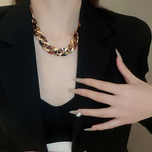 Detail of chunky gold and leopard print resin link necklace worn with black blazer