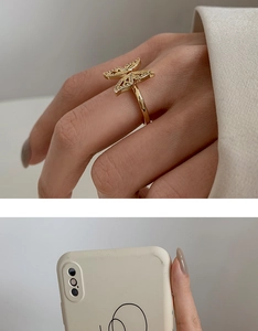 Detail of a golden butterfly ring with diamonds next to a cream-colored phone case