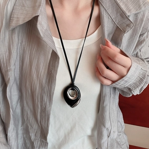 Detail of a black and silver water-drop pendant necklace worn on a grey shirt