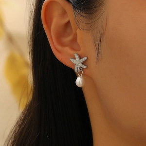 Detalle de pendientes de estrella de mar con circonitas brillantes y perlas de gota
