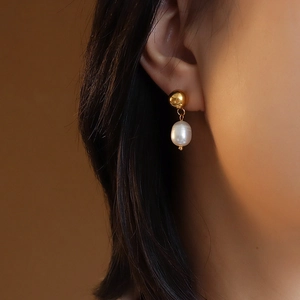 Elegant gold drop earrings with white teardrop pearls worn by a model in soft lighting