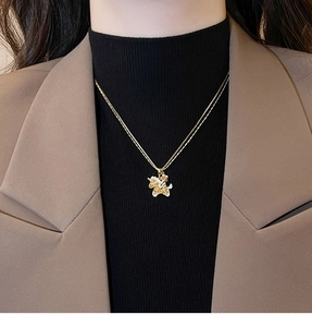 Close-up of a gold unicorn necklace with zircon crystals worn on a model with beige suit