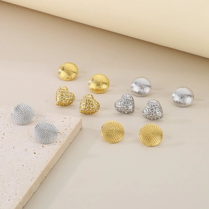 Detailansicht von Herz- und Textur-Ohrsteckern in Gold- und Silberfarben auf Stein