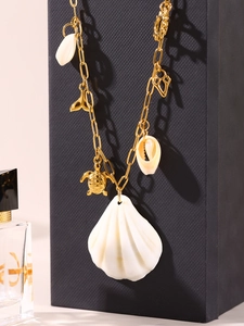 Detail of gold ocean-style necklace with natural white shell, sea turtle and fish tail charms