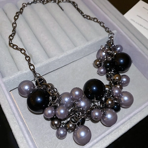 Close-up of irregular black and lilac cluster pearls on a dark metallic tassel chain