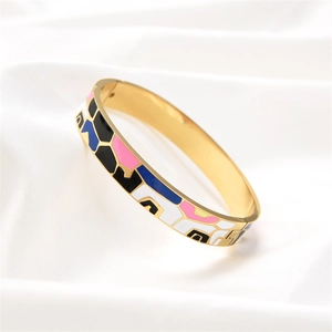 Detail of a gold stainless steel bangle with colorful geometric enamel inlays on white silk
