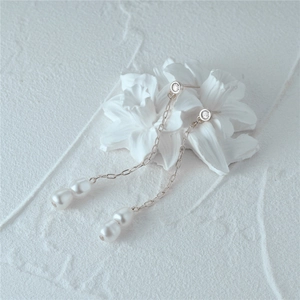 Detail of silver long chain pearl earrings featuring crystal studs and drops on white texture