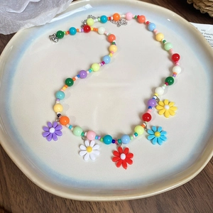 Close-up of colorful beaded necklace with five resin daisy flower charms in pastel tones