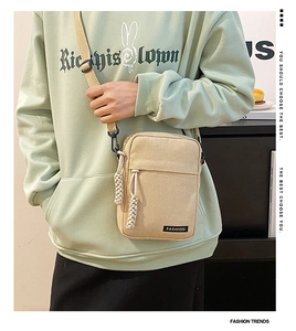 Close-up of beige canvas crossbody bag with FASHION label and woven rope zipper pull