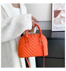 Detailed shot of bright orange shell bag with V-quilted texture and gold zippers