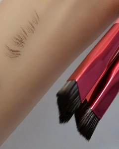 Detail view of red metal handle eyebrow brushes and dark makeup swatches on skin