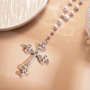 Detailed view of silver cross pendant with rhinestones on a white faux pearl chain
