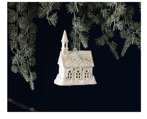 Detail of a cream church ornament with gold glitter hanging on a festive pine branch