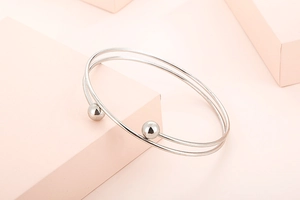 Close-up of minimalist silver stainless steel open bangle with bead ends on a pink block