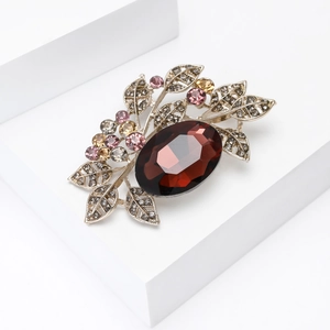 Macro shot of vintage gold leaf brooch featuring large red gemstone and pink crystals
