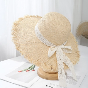 Detail of raffia sun hat with wavy fringe brim and white lace bow on wooden stand