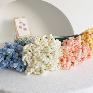 Fiori puff fatti a mano all'uncinetto in vari colori con steli verdi su tavolo bianco