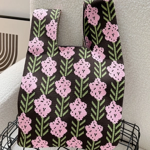 Close-up of knit tote bag with pink flower pattern on a textured cream sofa