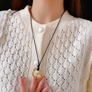 Close-up of a gold irregular geometric pendant on a black cord worn with a white knit top
