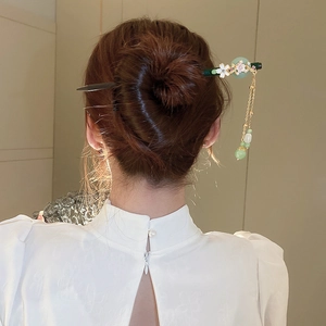 Detail of vintage flower hair pin with green pearls and metallic tassels on a bun