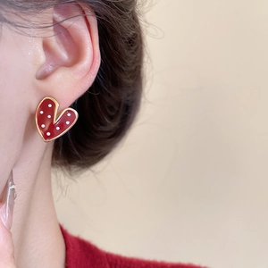 Close-up of heart-shaped red earrings with white polka dots and gold edges on ear