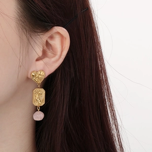 Detailed view of long gold earring with heart stud and pink natural stone on a model
