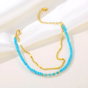 Close-up of double-layer gold chain bracelet with turquoise beads and heart charm