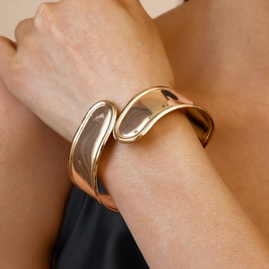 Detailed close-up of a wide polished metallic crossover bangle in a rose gold finish
