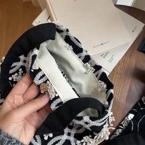 Detailed view of silver magnetic buckle and white embroidery on a black canvas bag