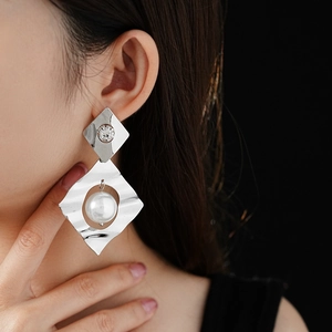 Close-up of geometric silver earrings with textured metal, diamond stud and pearl drop