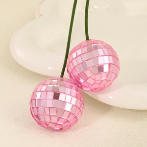 Creative pink disco ball cherry ornament with green leaves on a warm beige tray