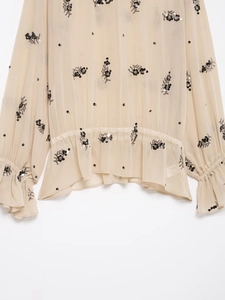 Detail of sheer beige blouse with black sequin flower embroidery and ruffled cuffs