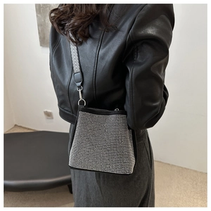 Détail d'un sac seau noir avec des clous argentés et une bandoulière tissée à chevrons