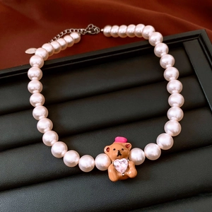Detailed close-up of pearl necklace featuring a brown bear pendant with heart-shaped gemstone