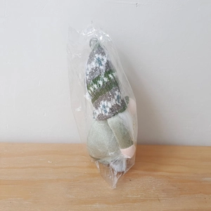 Detail einer grünen gestrickten Weihnachts-Wichtel-Puppe in transparenter Verpackung