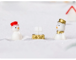 Miniature resin snowmen and golden gift box on simulated snow for holiday dioramas