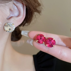 Detail of gold-plated stud earrings featuring large clear and pink crystal rhinestones