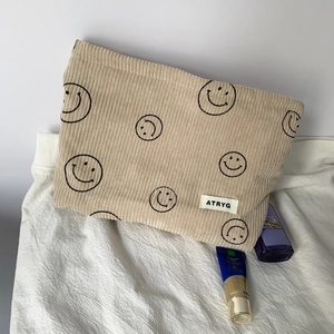 Detail of beige corduroy pouch with black smiley patterns and brand tag on white fabric