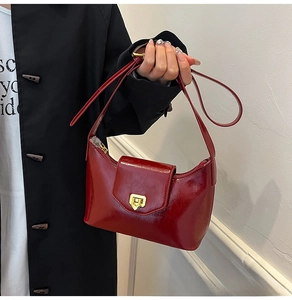 Detail of burgundy glossy leather handbag featuring a polished gold shield-shaped twist lock