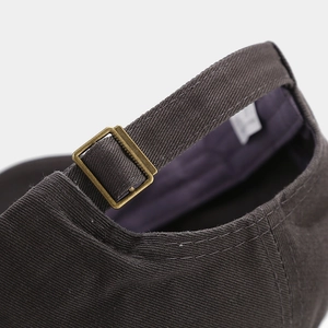 Detail of the dark brown cotton baseball cap featuring an adjustable bronze metal buckle back