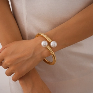Detail of a gold spiral cuff bracelet with large pearls on a silk sleeve background