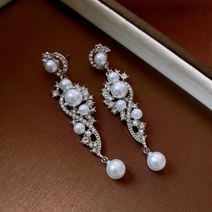 Macro shot of silver pearl long drop earrings with crystals on dark textured surface