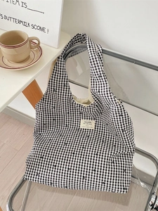 Minimalist black and white plaid canvas tote bag resting on a chair in a cozy setting