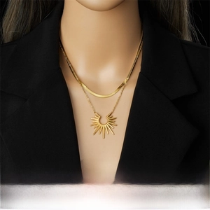Detail of a double-layered gold sunflower necklace with a sleek snake chain on a black suit