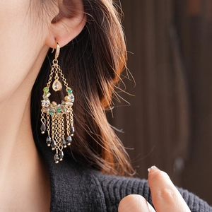 Detailed view of long tiered tassel earrings with green and black beads on gold chains