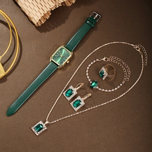 Flat lay of women's jewelry set with emerald quartz watch and gold accessories