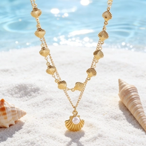 Dettaglio di collana dorata a due strati con conchiglie e perle sulla sabbia bianca