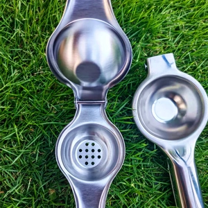 Detail of stainless steel manual lemon squeezer with hinge and filter on green grass