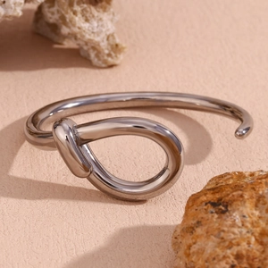 Polished silver twisted hollow teardrop cuff bracelet on natural sand and stone