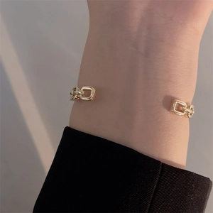 Detail shot of a golden open-cuff bracelet with chain links worn on the wrist